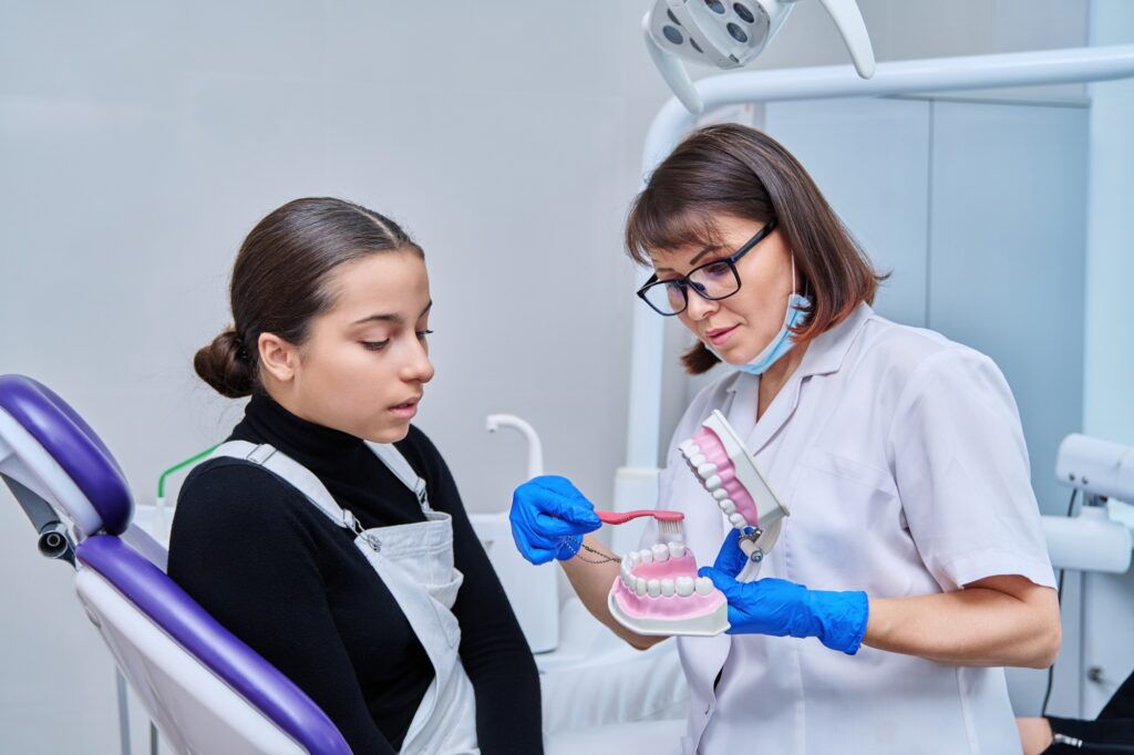Teenage female patient learning oral hygiene from a doctor with a jaw model and toothbrush at HCT Dental Clinic, a top Dental Centre Turkey in Antalya.
